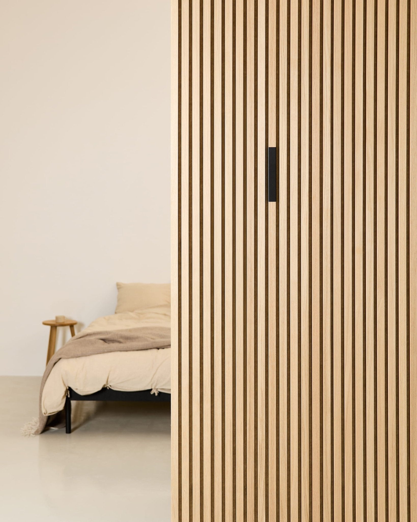 Minimalist bedroom featuring a beige bed, wood side table, and WoodUpp Liva Black Aluminum acoustic panel adding texture to the vertical partition.