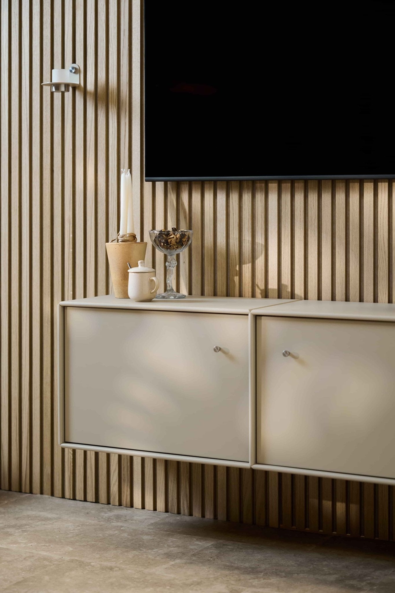 Minimalistisk stue med WoodUpp Arka TV-kommode i beige, Akupanel akustisk træpanelveg, vægmonteret TV, stearinlys, glasskål, hvid krukke og pænt arrangerede kabler.