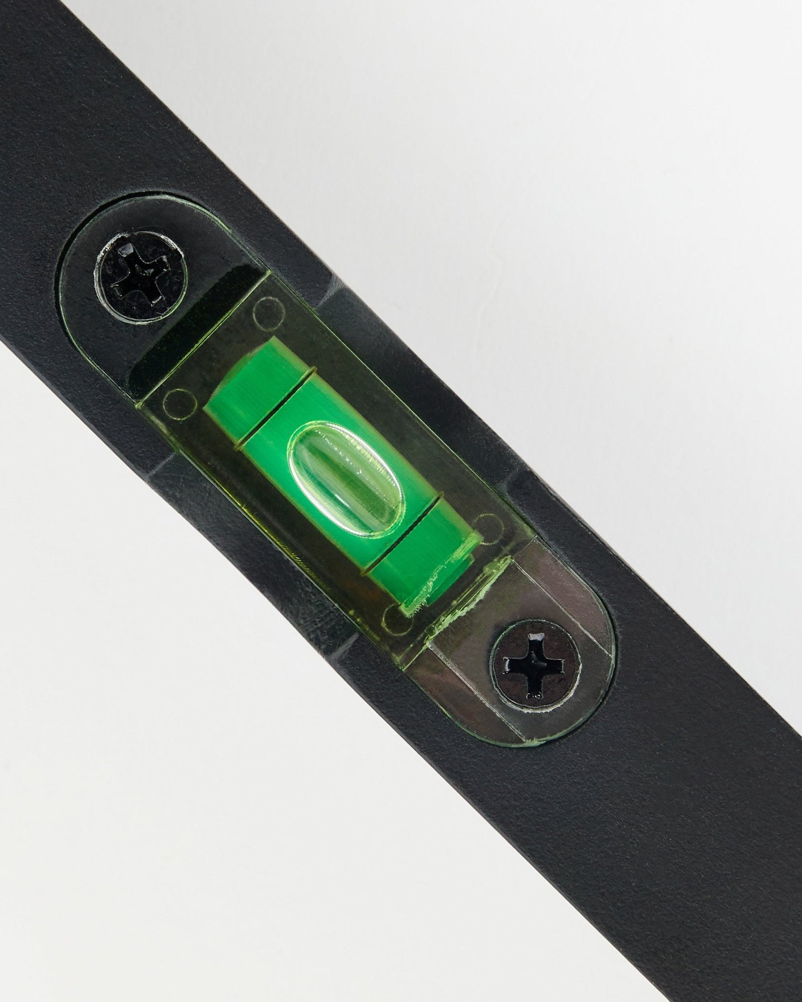 Close-up of a black WoodUpp spirit level (15 x 3.2 cm) with green vial, used for precise installation of acoustic panels.