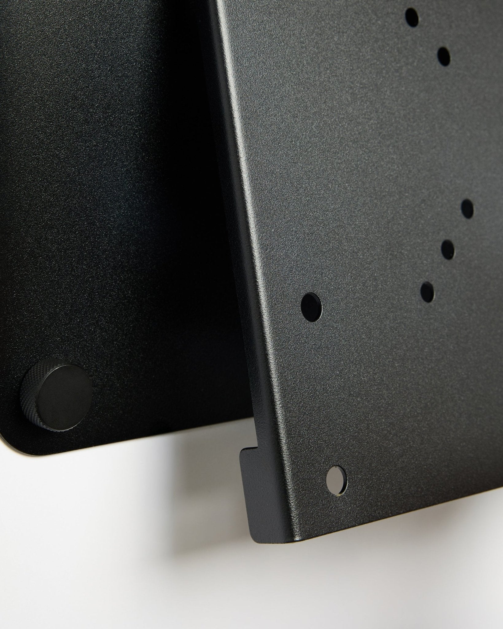 Close-up of the Fjell TV Mount (small) by WoodUpp, a black metal bracket with circular holes and adjustment knob, displayed against a white background.
