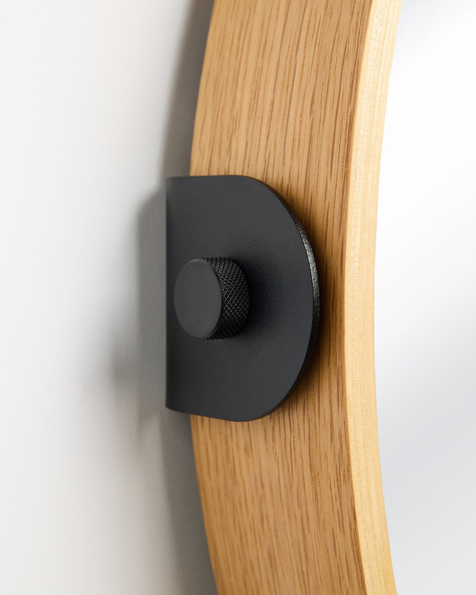 Detail of the WoodUpp Linn Mirror in Natural Oak, an acoustic panel mounted to the wall with a black metal bracket and round knob.