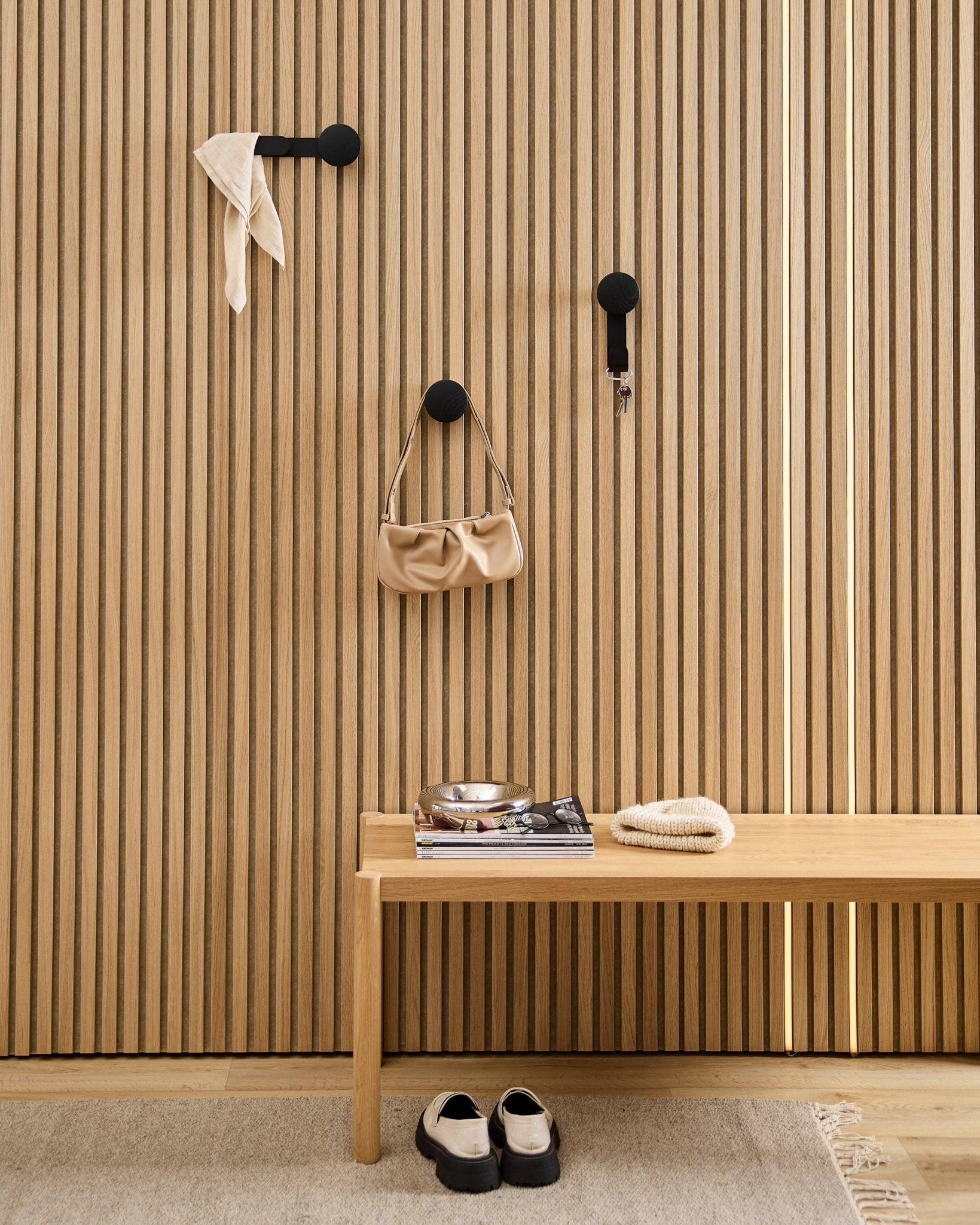 Minimalist entryway featuring a WoodUpp Linn Horizontal Hanger in Black Oak with black hooks, wooden bench, shoes, books, and a dish. Nordic style.