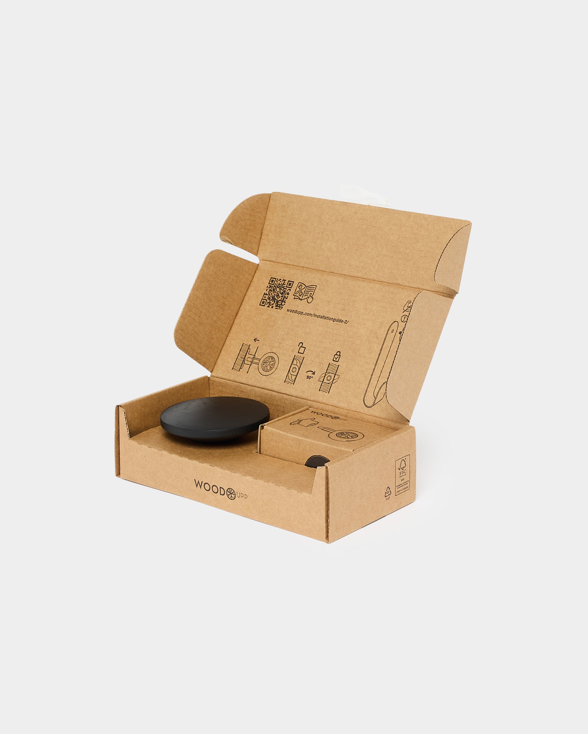 A compact black accessory from WoodUpp’s CREATE collection sits in an open brown cardboard box displaying printed instructions on the inner lid.