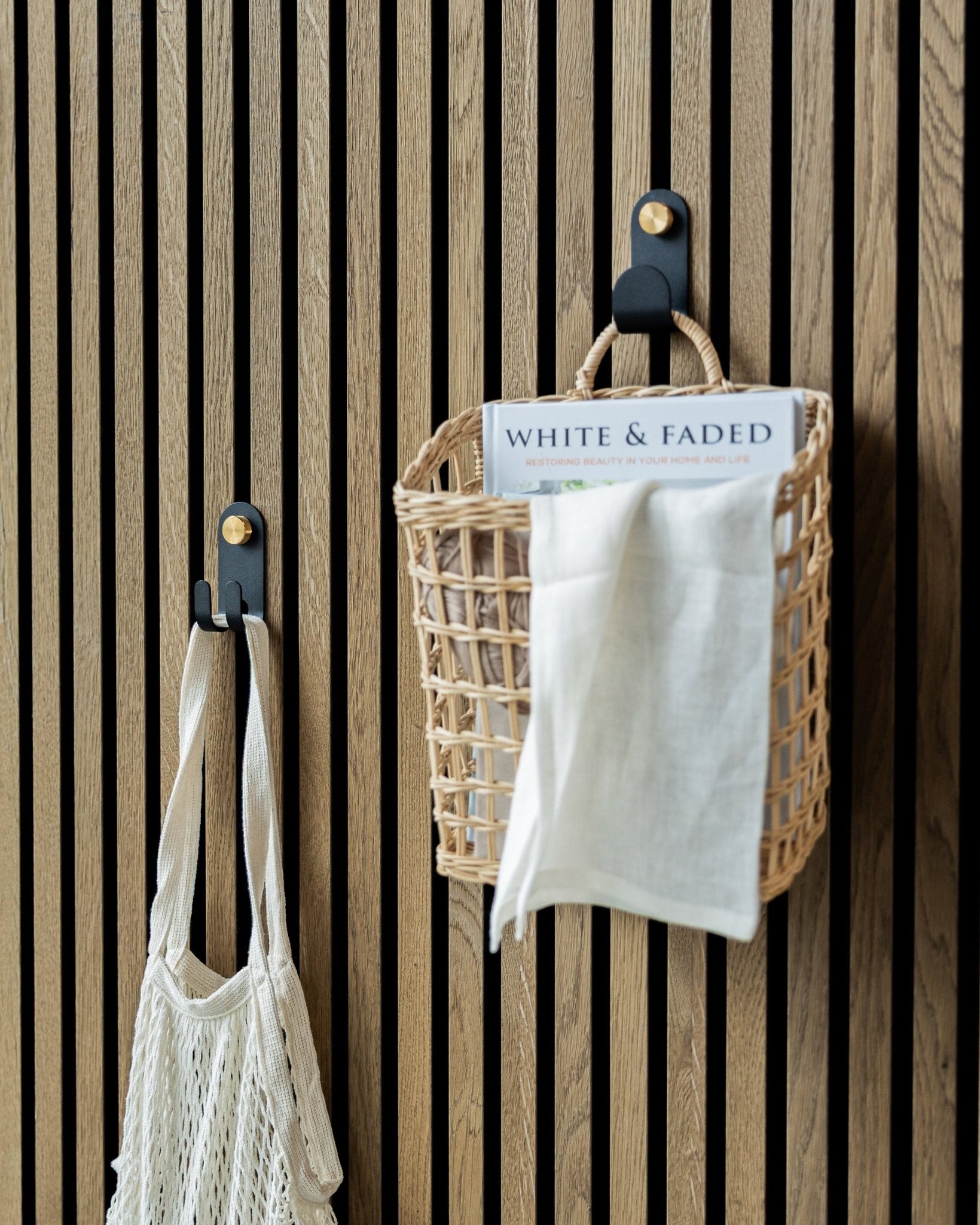 WoodUpp’s Norr Single Hanger in Black holding a woven basket and mesh bag mounted on a Nordic acoustic slatwall panel for organized storage.