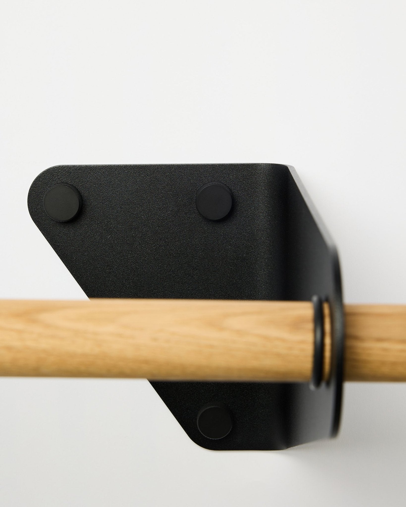 Close-up of the WoodUpp Linn Coat Rail in black, 115.9 cm, installed on a white wall with a triangular metal bracket, shown as part of Nordic acoustic accessories.