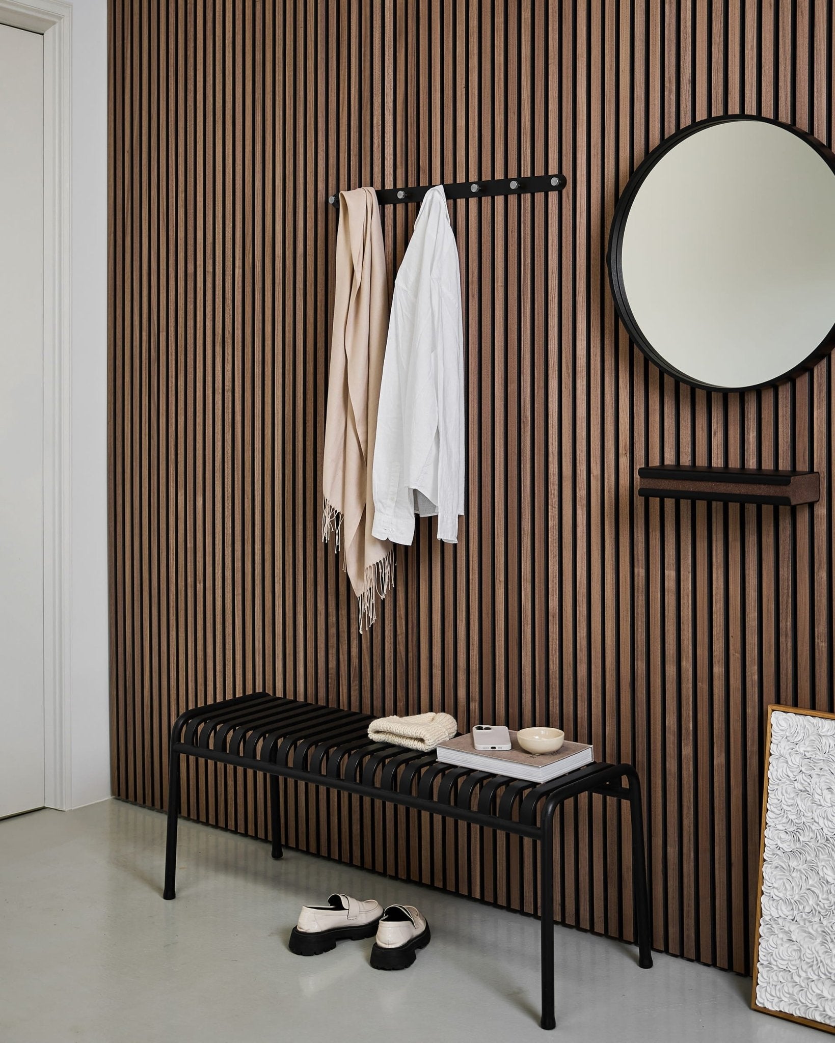 Modern entryway with a Nordic slatted acoustic wood panel wall, round mirror, black bench, WoodUpp Norr Coat Hook Rack, and slippers on a light floor.