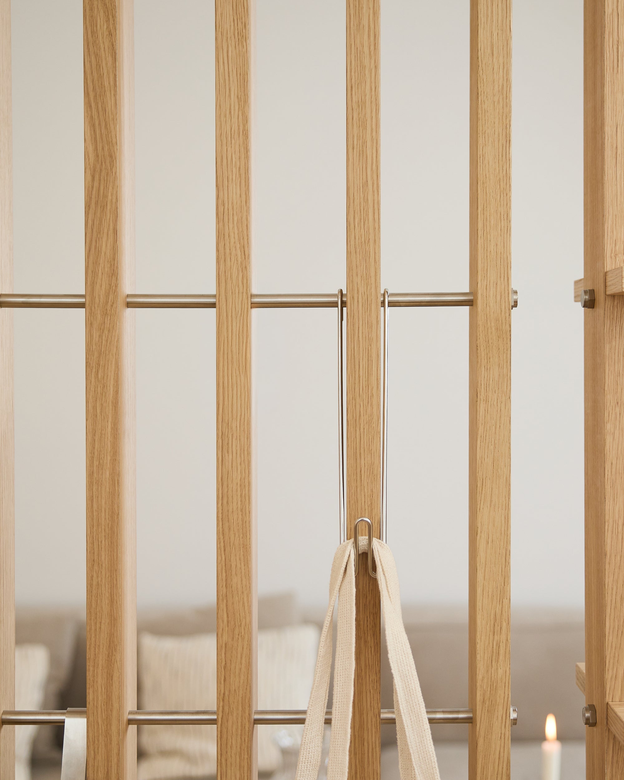 Light wood gate with metal bars, beige tie, and three WoodUpp Alva Wire Hooks/BM1; blurred sofa and candle in the background.