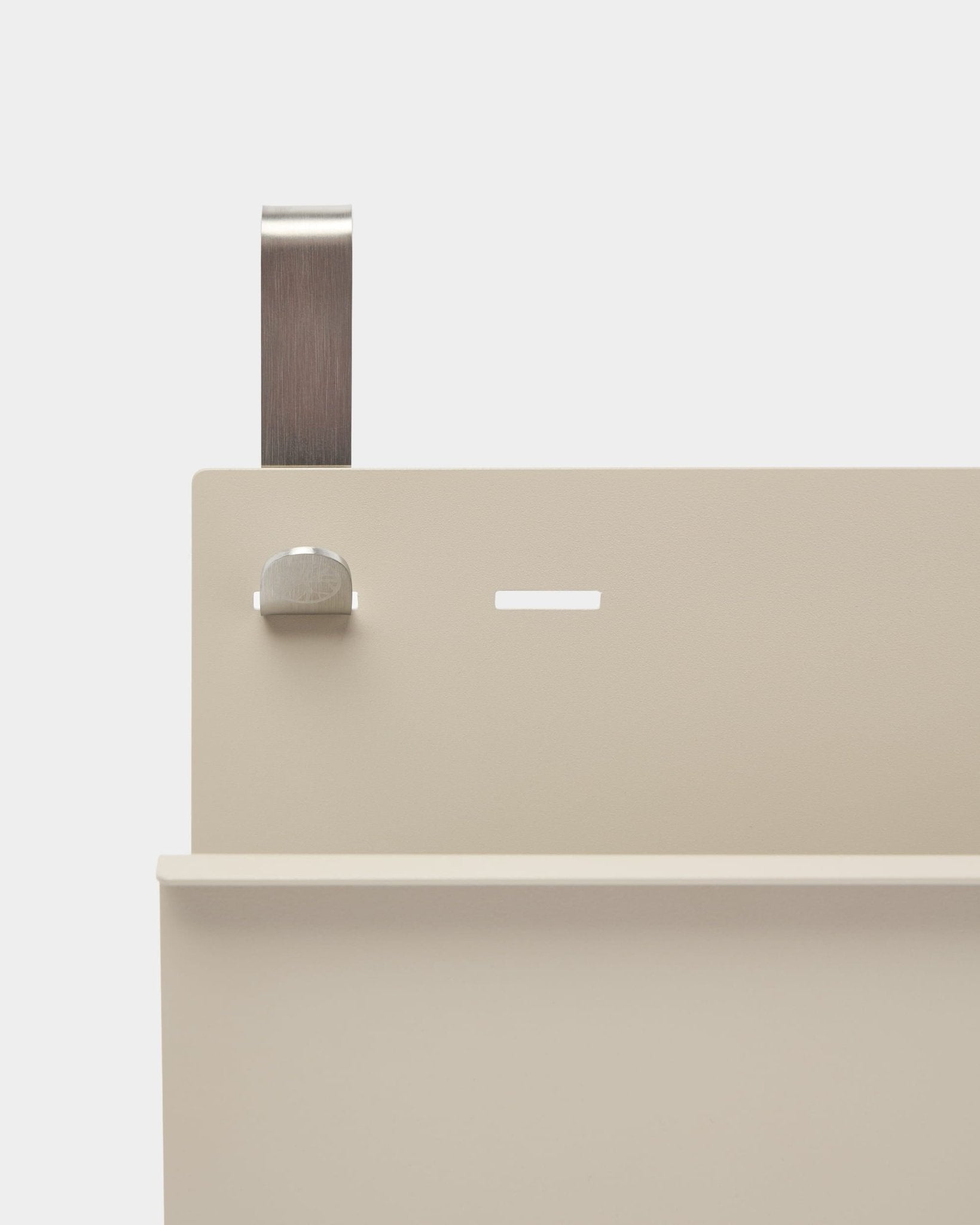 Close-up of WoodUpp Nell magazine storage in beige powder-coated steel with shelf, slot, bolt, and curved handle; functions as room divider or magazine holder.