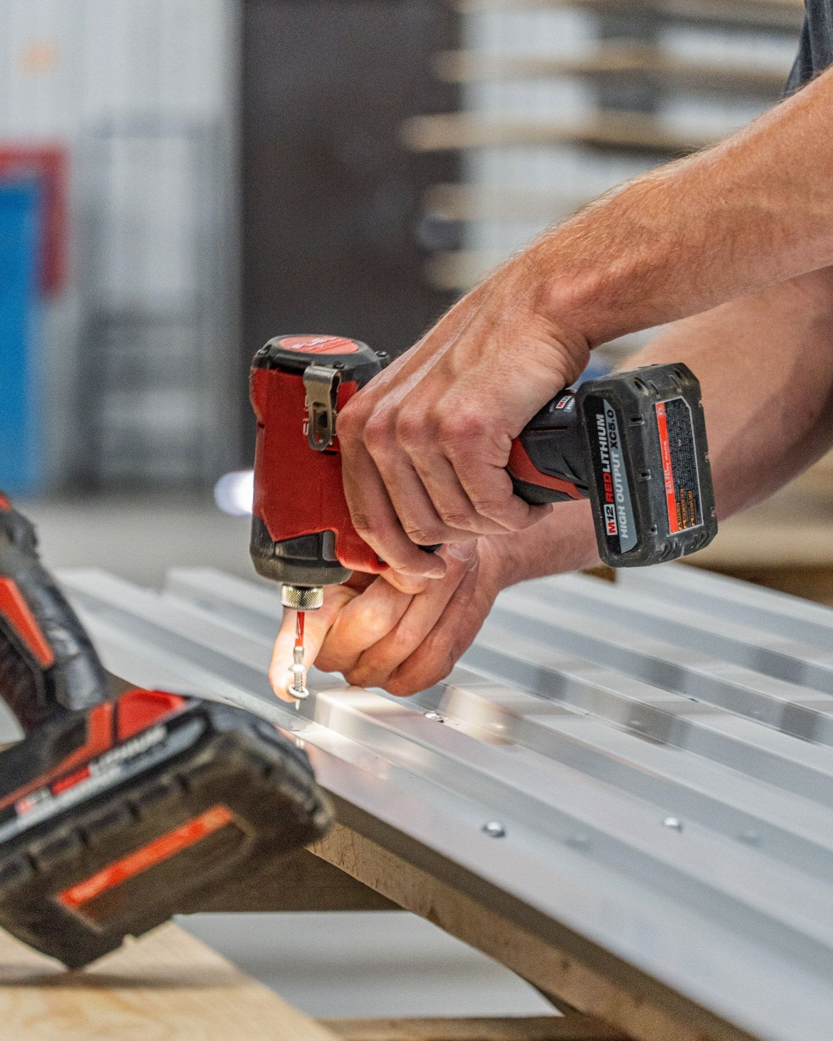 A person installs WoodUpp Backside Screws 4.8x19 with Ø10 washer TX20 (black) to attach acoustic panel fixings into sheet metal on a workbench.