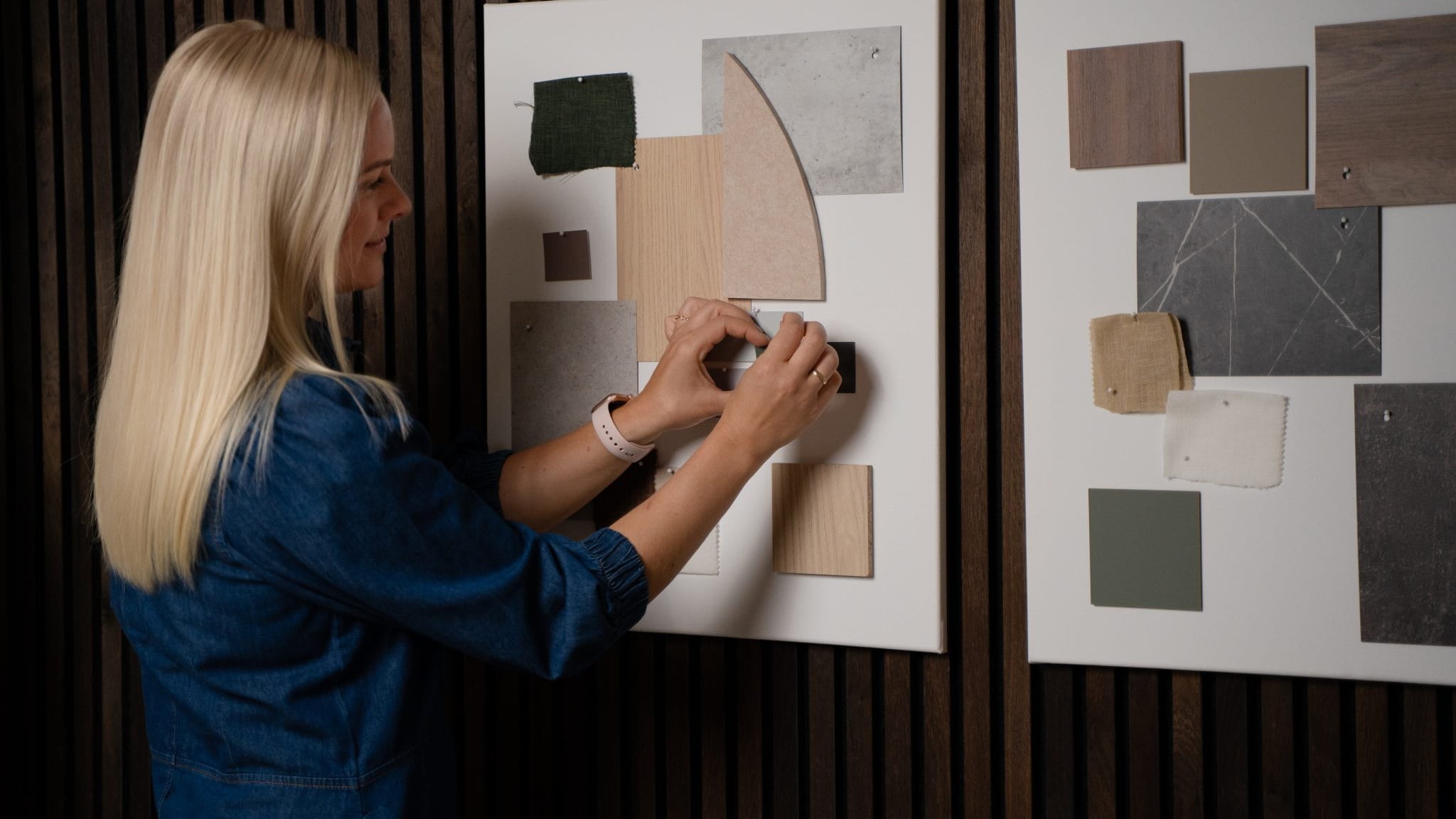 A woman arranges fabric and color samples on a mood board, with another inspiration board beside her, near acoustic wood panels from WoodUpps Akupanel collection.