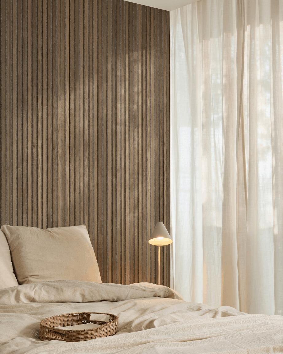 Minimalist bedroom featuring beige bedding, a wicker tray, WoodUpp Akupanel Rustic Grey Oak acoustic slatwall panel, a white lamp, and sheer curtains.
