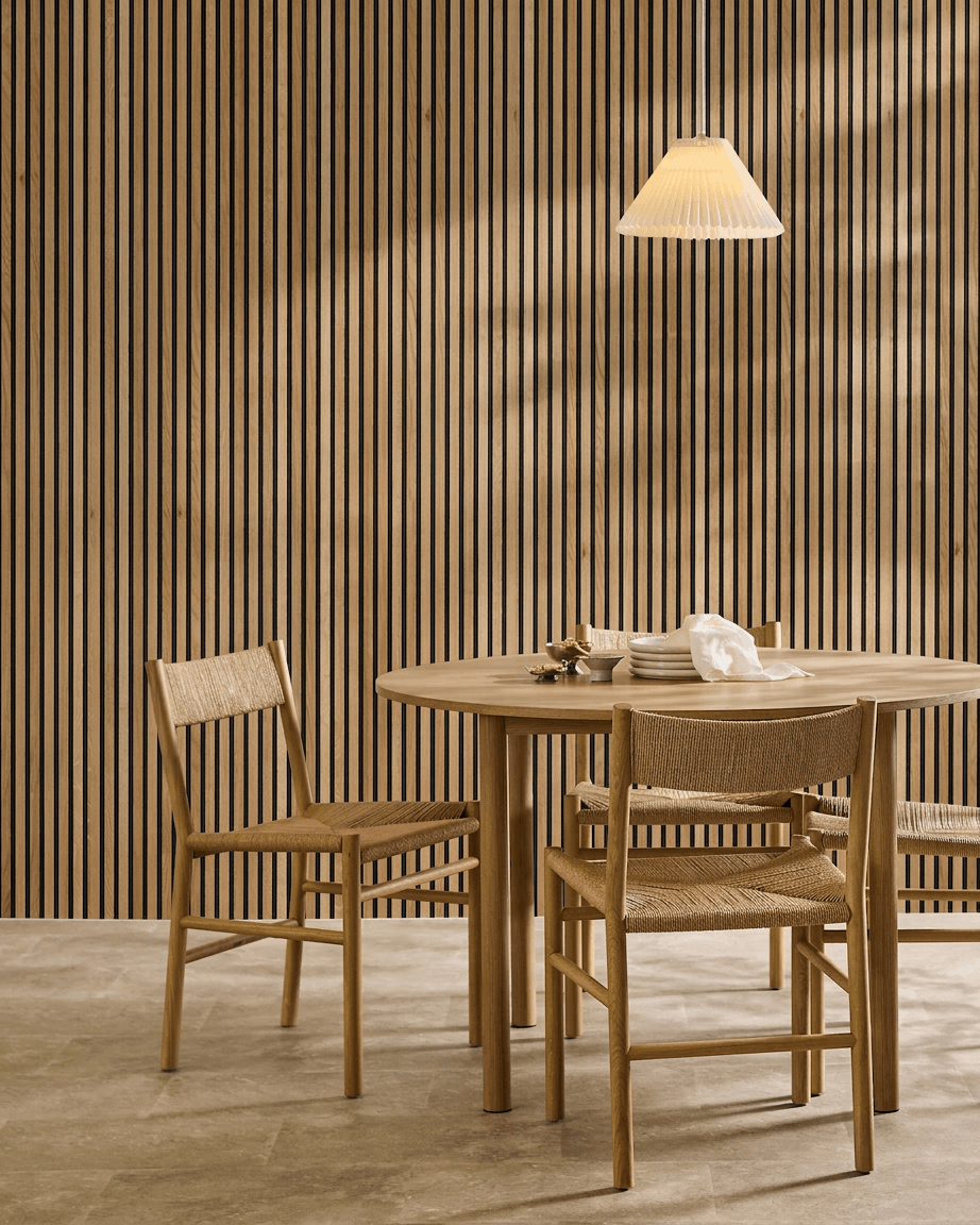 Minimalist dining area with a round table, woven chairs, and WoodUpp Akupanel acoustic slatwall panel in Rustic Natural Oak as a Nordic wall accent.