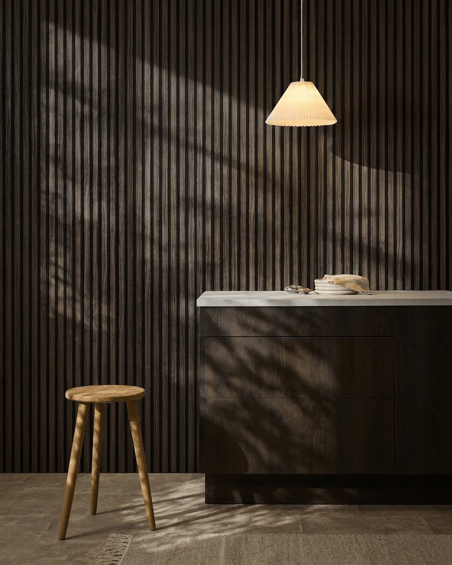 Minimalist kitchen with WoodUpp Akupanel Black Oak acoustic panels on the wall, wooden stool, white countertop, beige pendant lamp, and sunlit shadows.