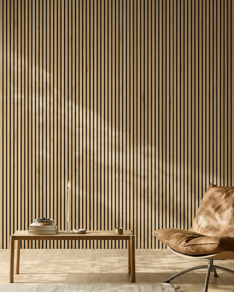 Sunlight illuminates a modern room with a WoodUpp Akupanel Acoustic Panel in Rustic Natural Oak on the wall, alongside a tan leather chair and minimalist bench.
