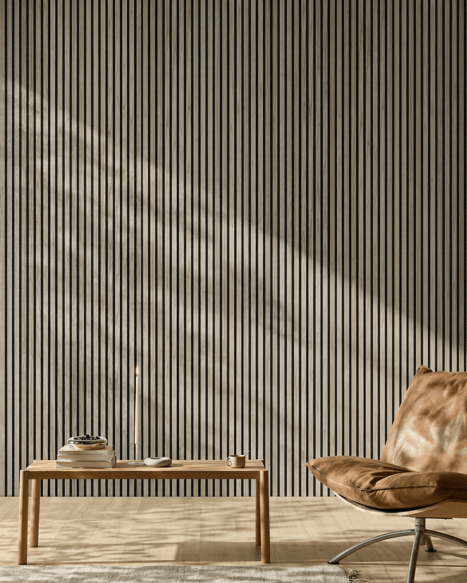 Minimalist room featuring a 240x60cm WoodUpp Akupanel in Weathered Oak with black felt, wooden bench, books, candle, cup, and tan leather chair.