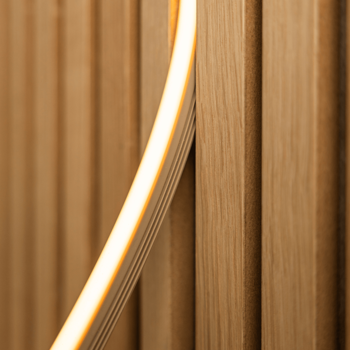 Close-up of WoodUpp Lumi LED striplight in beige (240cm) emitting warm yellow light onto Akupanel vertical acoustic wood slats; Philips Hue compatible.