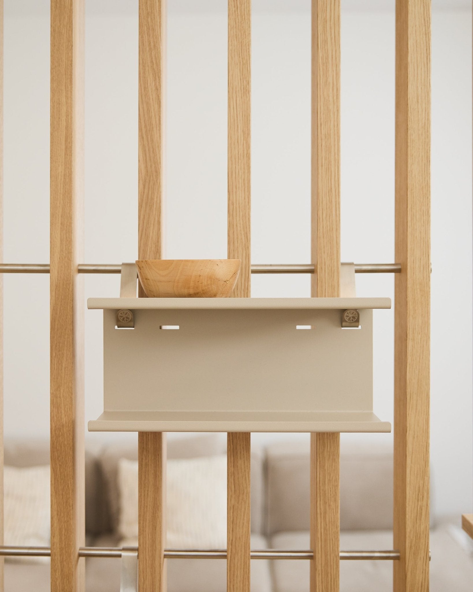 A small wooden bowl on the beige Nell Double Metal Shelf by WoodUpp (31.7 cm), with a blurred sofa and cushions in the background.